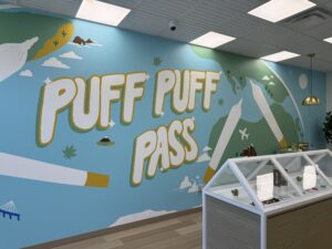 A colorful mural titled "Puff Puff Pass" by Calgary Mural Artist Kiran Rai-Bhullar, founder of Kinn Studios for Bud Mart Cannabis. This mural is a play on words that celebrates global cannabis culture.