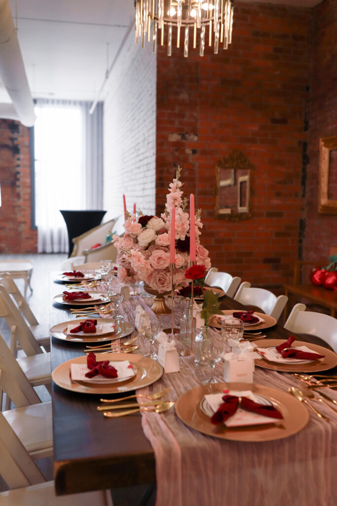 Overhead view of Ma Chérie bridal shower tablescape by Kinn Studios in Calgary, featuring a blush-pink linen runner, gold charger plates, red velvet napkins, floral centerpieces and custom merci favor boxes