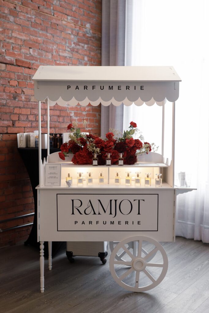 Custom Ramjot Parfumerie cart at Ma Chérie bridal shower in Calgary by Kinn Studios, with scalloped canopy, red rose garland and personalized signature perfume bottles