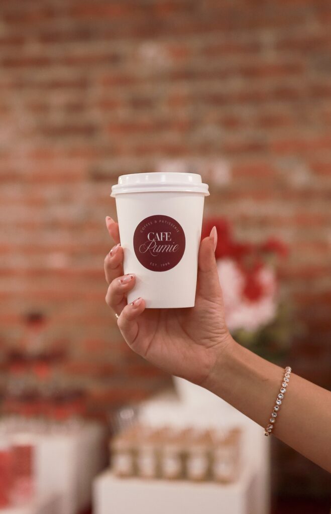 Kinn Studios event designer holding a Café Rumie branded cup at the Ma Chérie gluten-free bridal shower in Calgary against an exposed brick backdrop